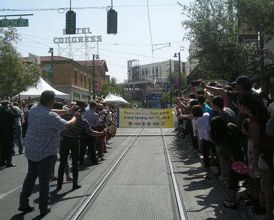 Jubilant crowd lines track for photo-op moment as Tucson's first modern streetcar approaches inauguration banner on opening day. Photo: Ed Havens.
